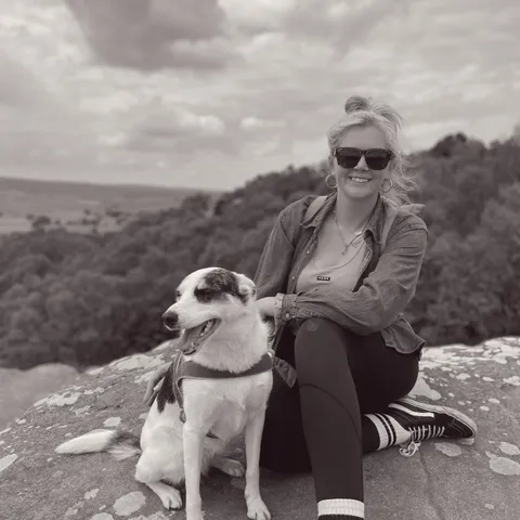 Abby kneeling on rocky outcrop with Luna against hills and water