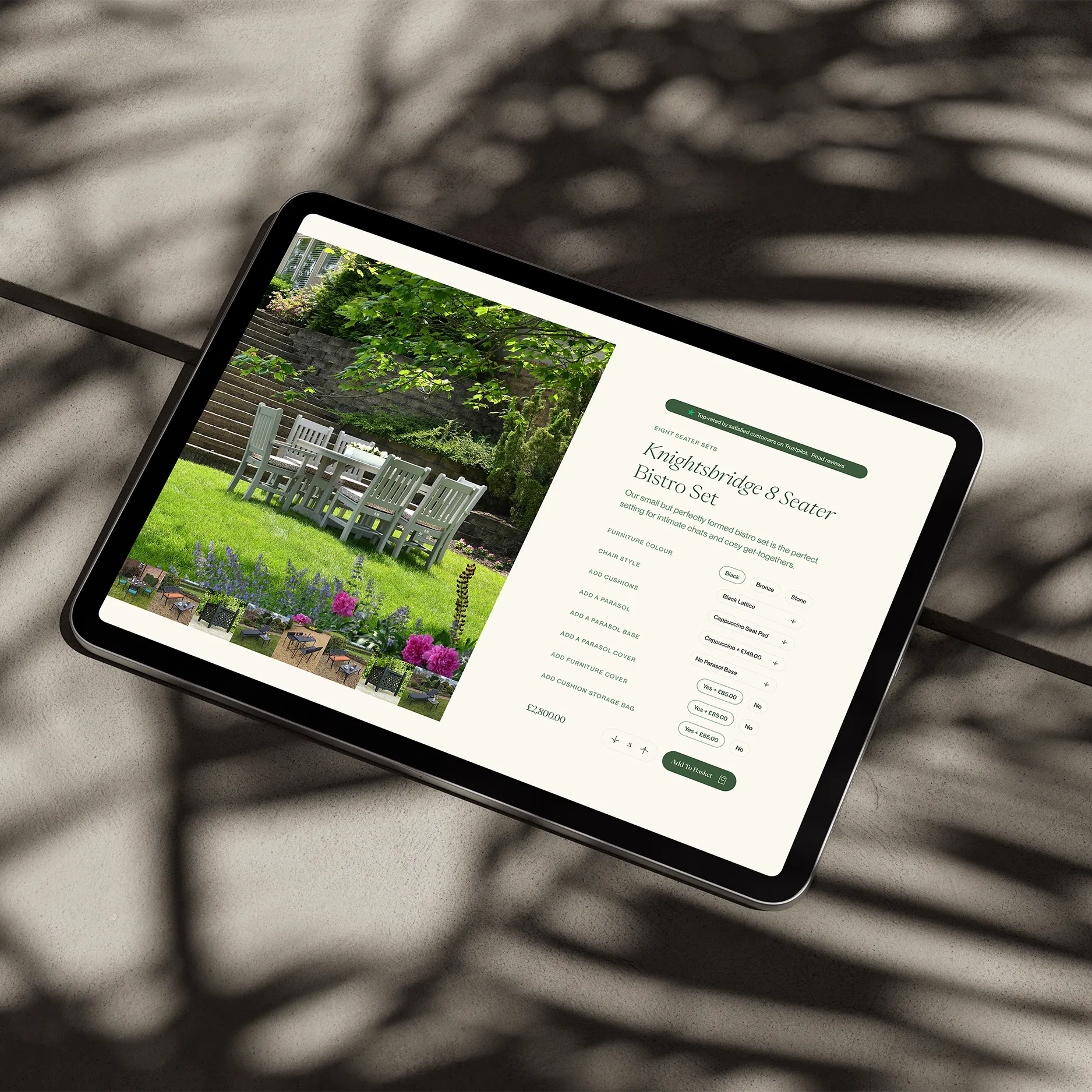 Tablet displaying a product page for the Knightsbridge 8 Seater Bistro Set, placed on stone with leafy shadows