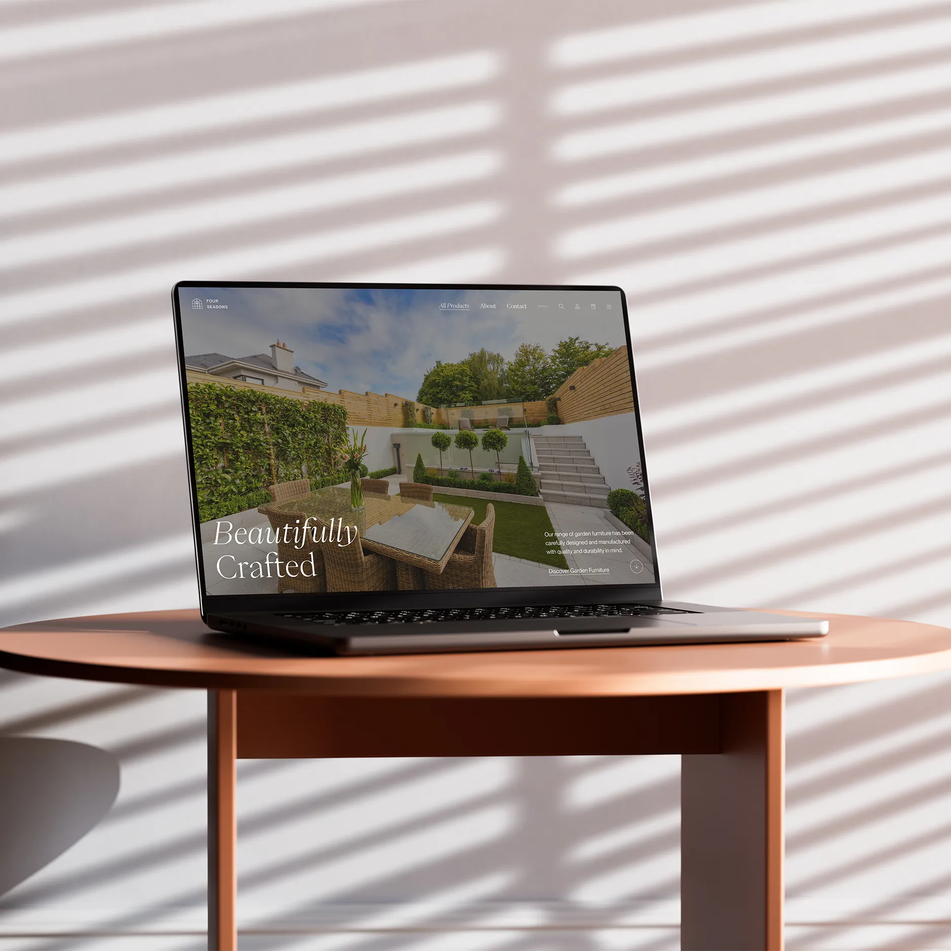 Laptop on a wooden table showing a website with modern garden furniture and a landscaped outdoor space