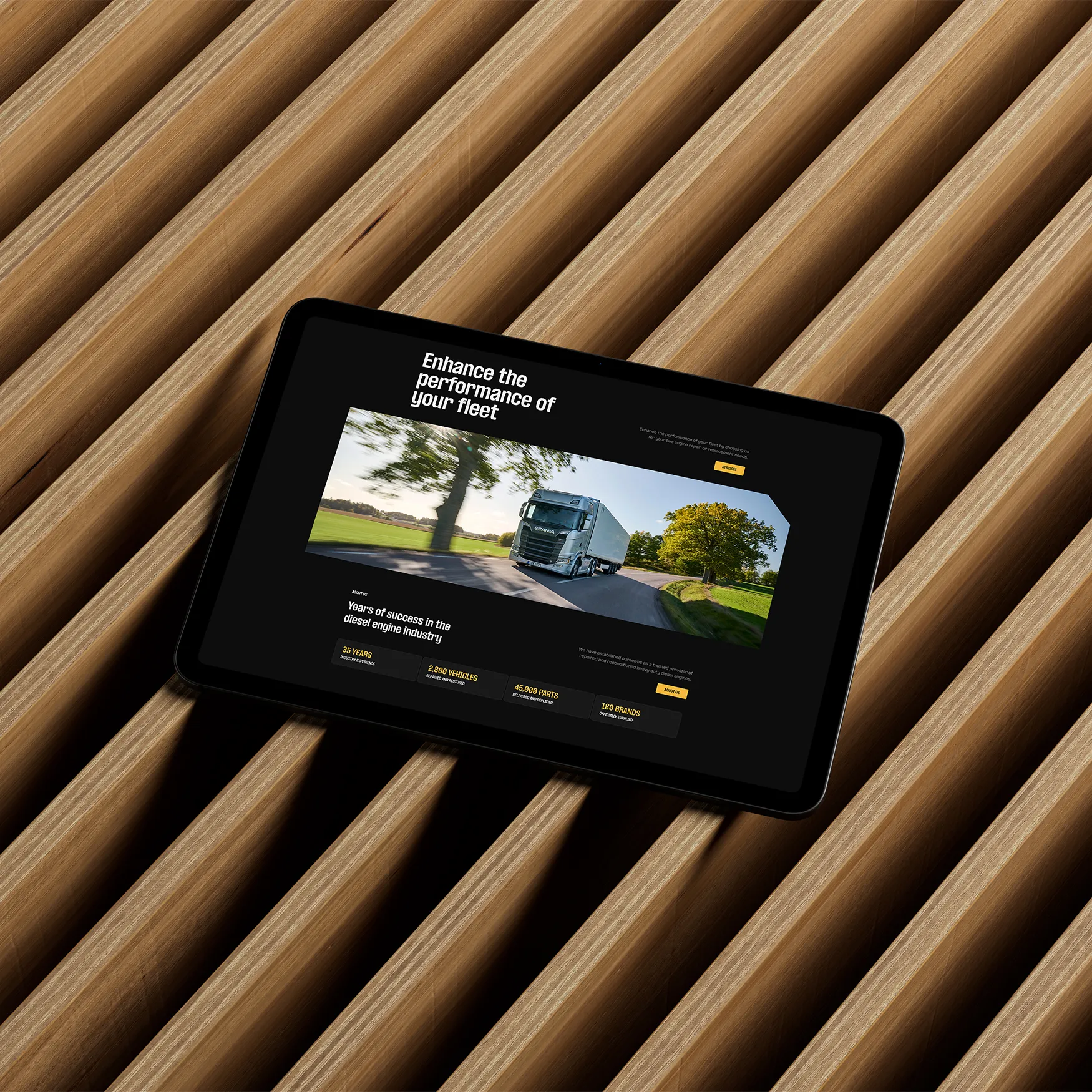 Tablet on a wooden slatted surface showing a trucking fleet website with a highway scene and performance statistics