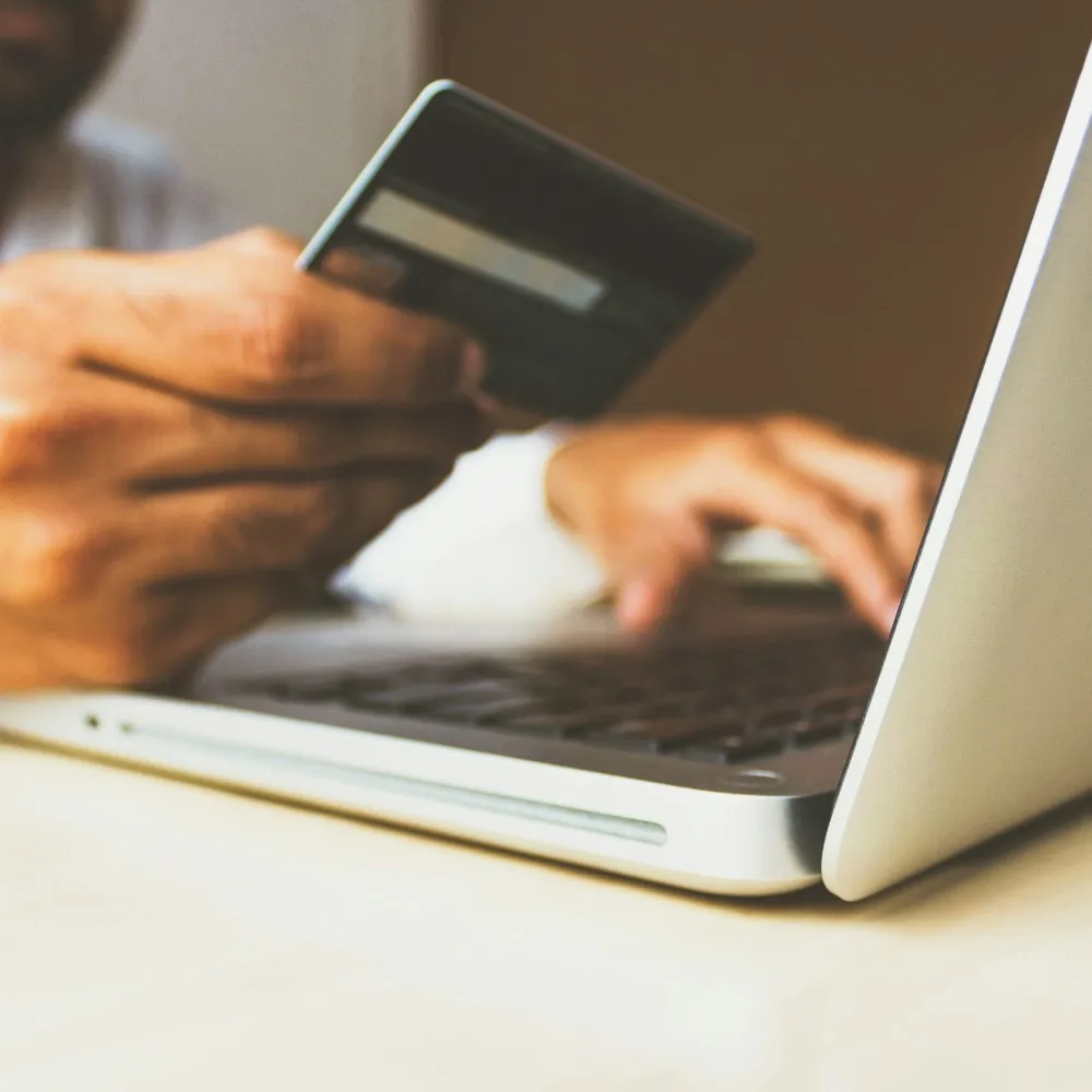 A man holding a credit card typing on a laptop