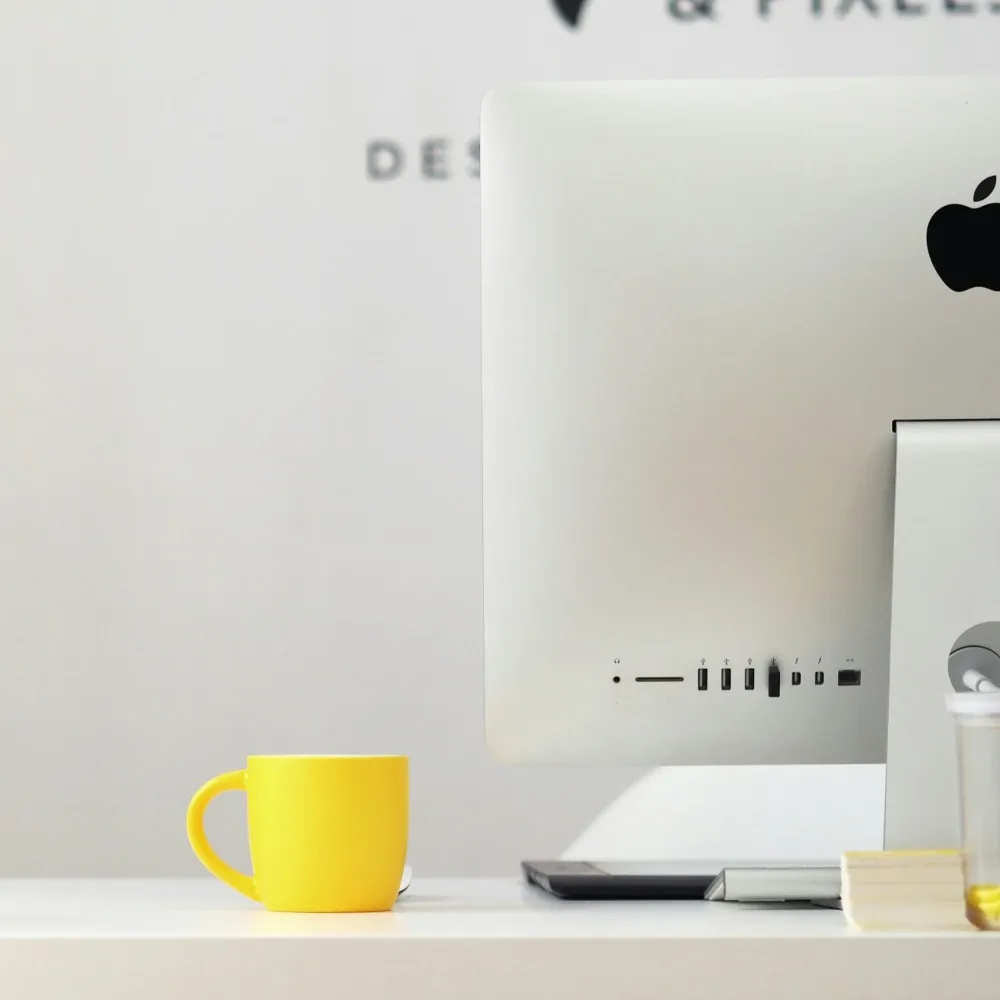A mac desktop computer with a yellow cup next to it